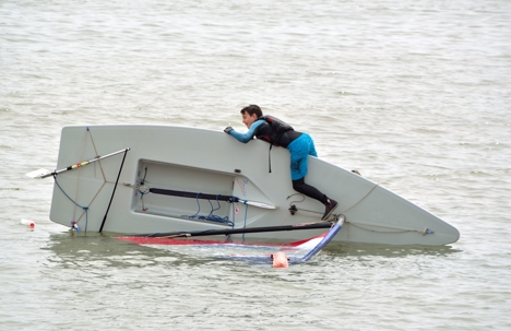 young man clings onto capsized sailing dinghy at sea in Felixstowe Suffolk England